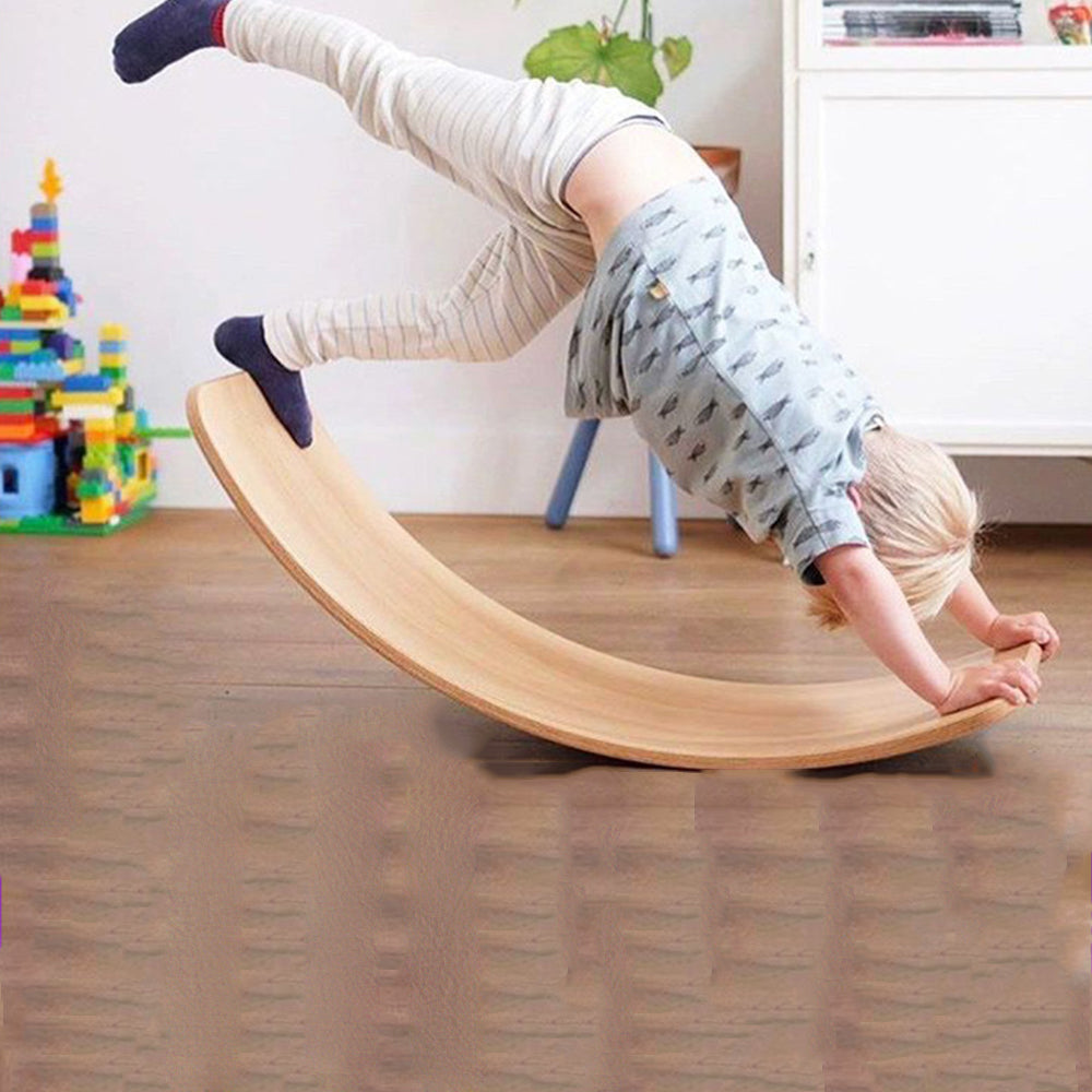 Ein Junge macht einen Handstand auf einem natürlichen Holz-Wackelbrett im Innenbereich.