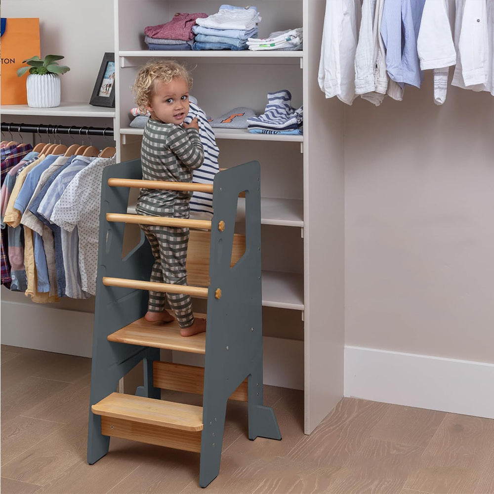 Faltbarer Montessori-Lernturm aus naturbelassenem und grauem Holz mit gelbem Blumendetail – ideal für Kleinkinder bei Aufgaben in Küche und Bad