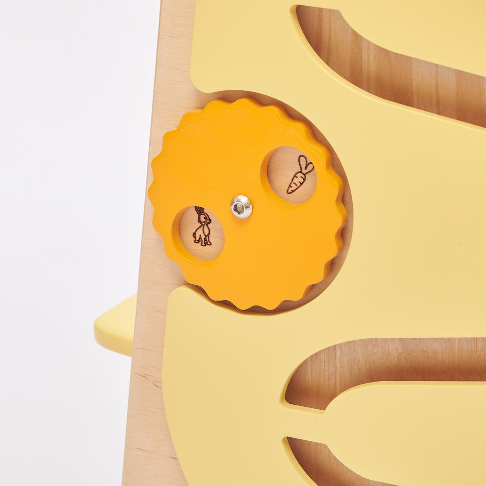 Montessori Lernturm aus Naturholz mit gelbem seitlichem Busy Board, ausgestattet mit interaktiven Zahnrädern, Schiebereglern und verschließbaren Elementen für Kleinkinder.