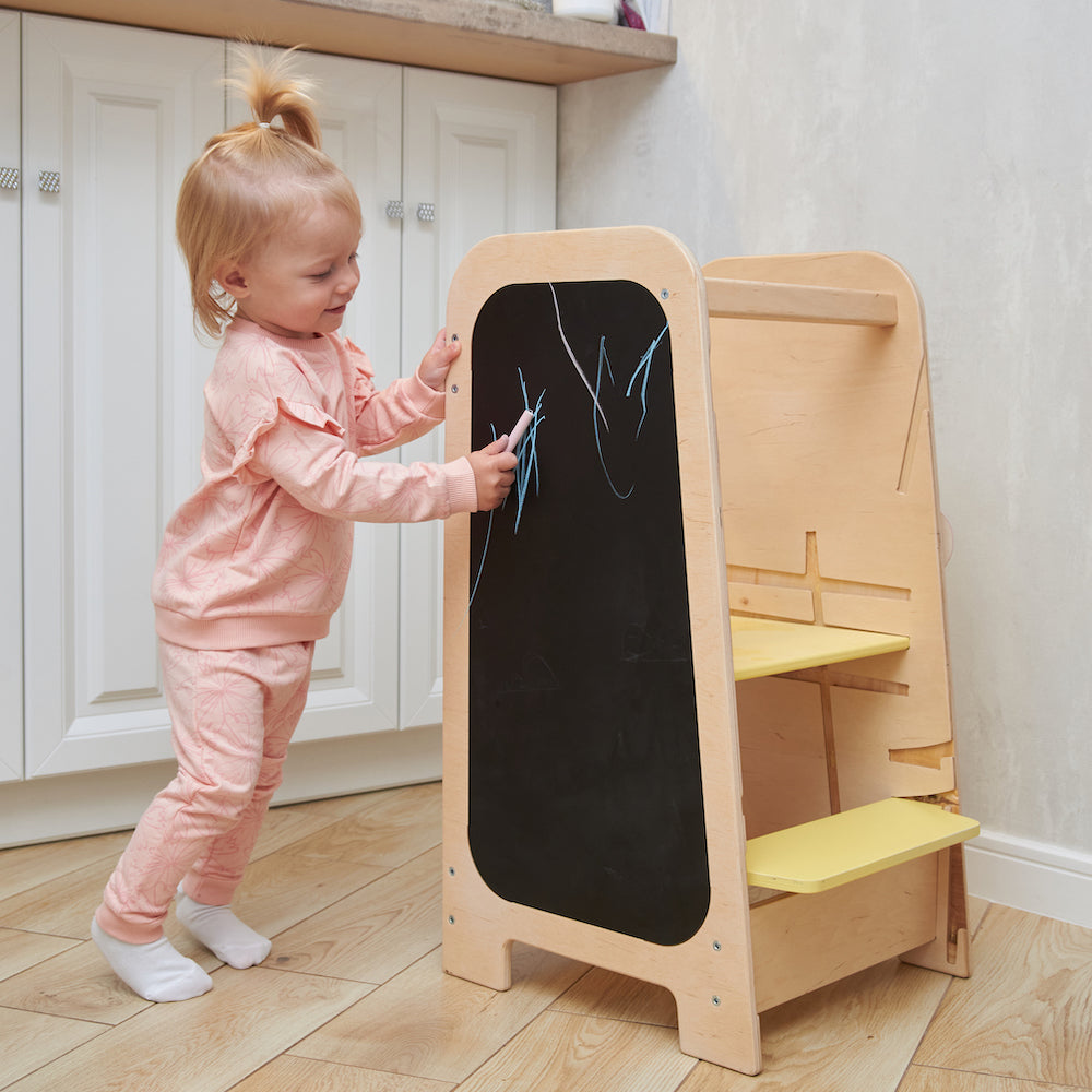 Montessori Lernturm aus Naturholz mit gelbem seitlichem Busy Board, ausgestattet mit interaktiven Zahnrädern, Schiebereglern und verschließbaren Elementen für Kleinkinder.