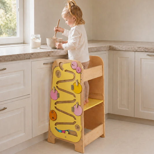 Kind nutzt den Montessori Lernturm mit Busy Board am Küchentresen