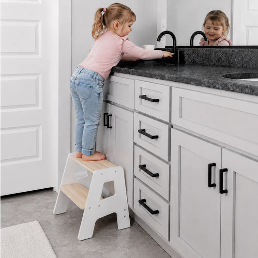 Toddler standing on a wooden step stool helping in the kitchen