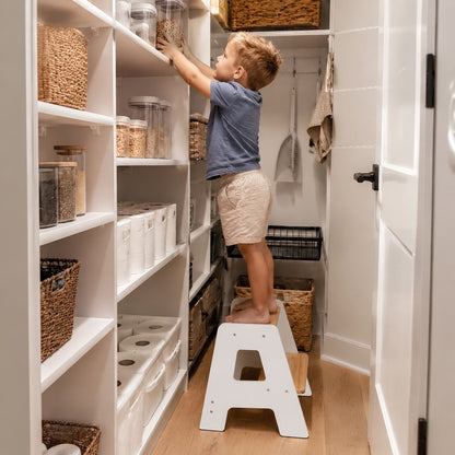 Child using a kids step stool to reach shelves and organize items