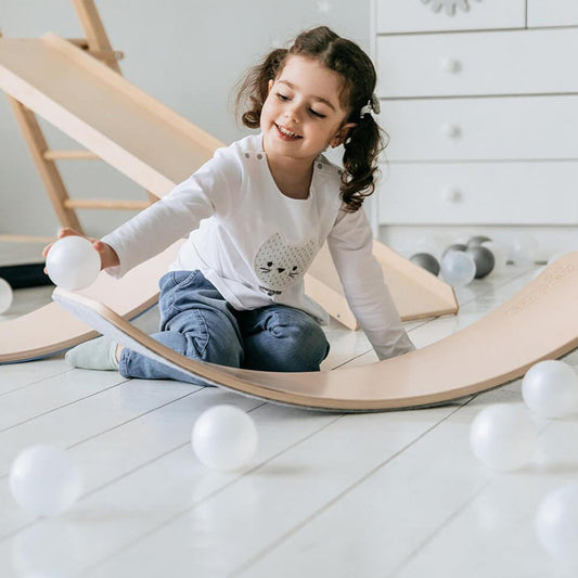 Kinder stehen und balancieren auf gebogenen Holz-Wackelbrettern für sensorisches Spiel.